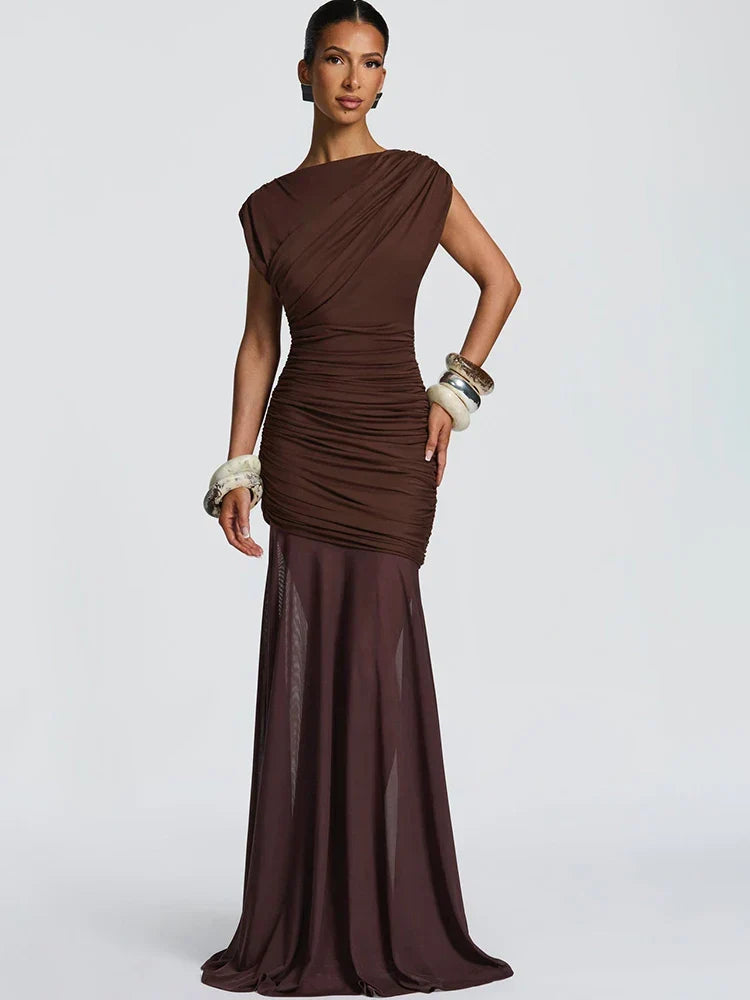 Elegant brown gown with ruched design and sheer skirt, worn with chunky bracelets in a studio setting.