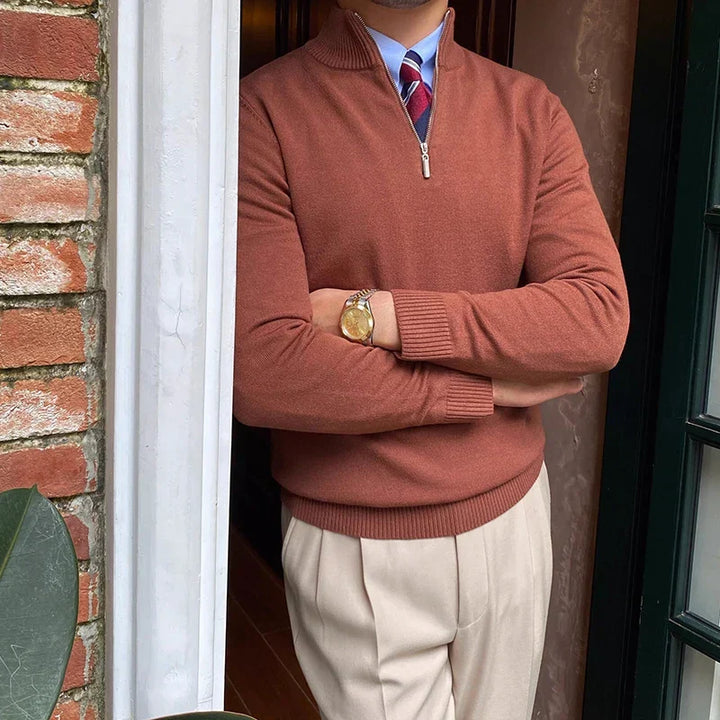 Rust-colored half-zip sweater with shirt and tie, worn with beige trousers near a brick wall and door.