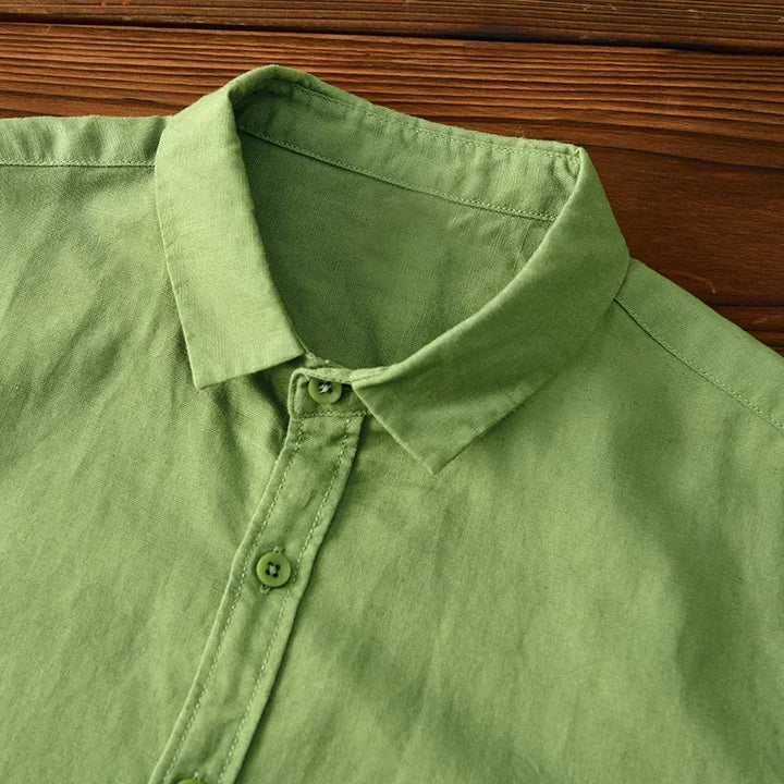 Close-up of green linen shirt collar and buttons on wooden surface.