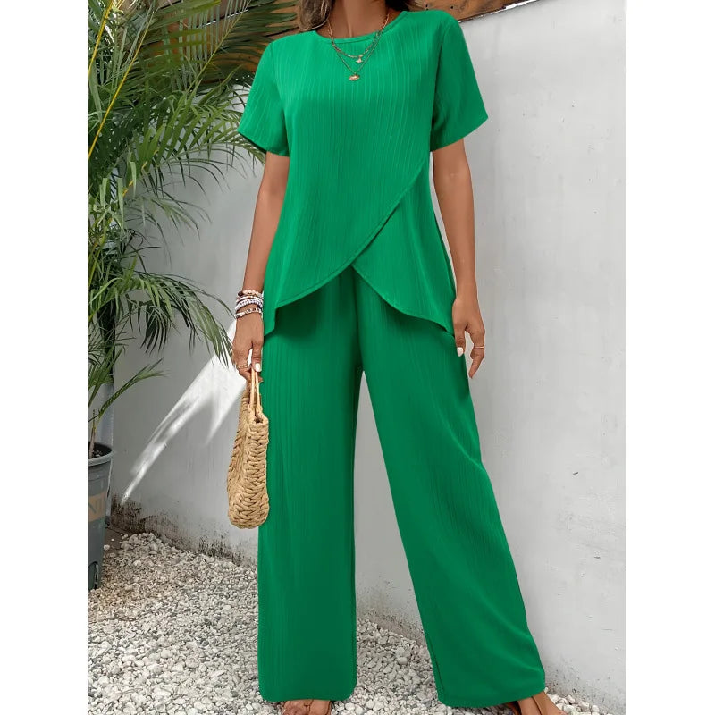 Green two-piece set with soft, flowing short-sleeve top and wide-leg pants, modeled outdoors with tropical plants.