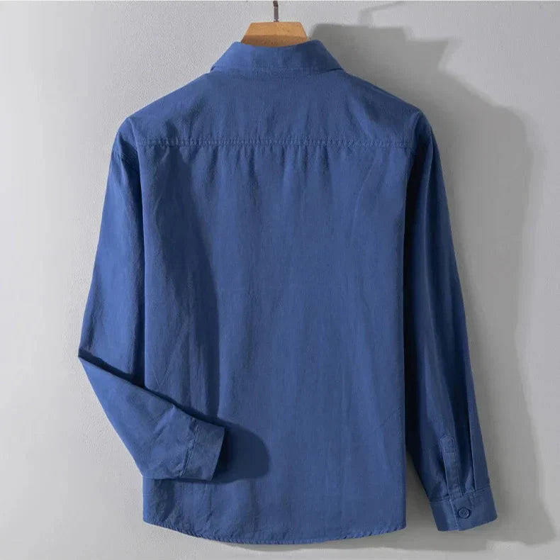 Back view of deep blue shirt with long sleeves on wooden hanger, gray studio background.