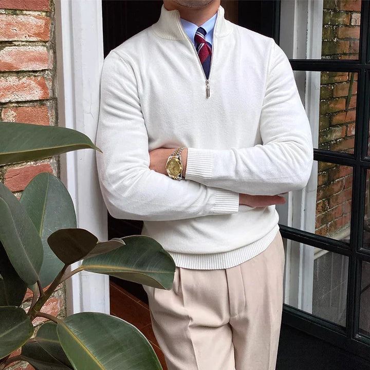 White half-zip sweater with shirt and tie, worn with beige pants, against a brick and glass door backdrop.