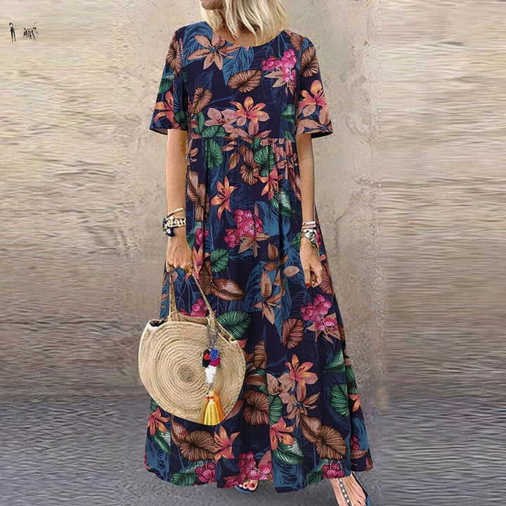 Model wearing a navy floral dress with colorful leaves, holding a woven round bag, set against a textured wall background.