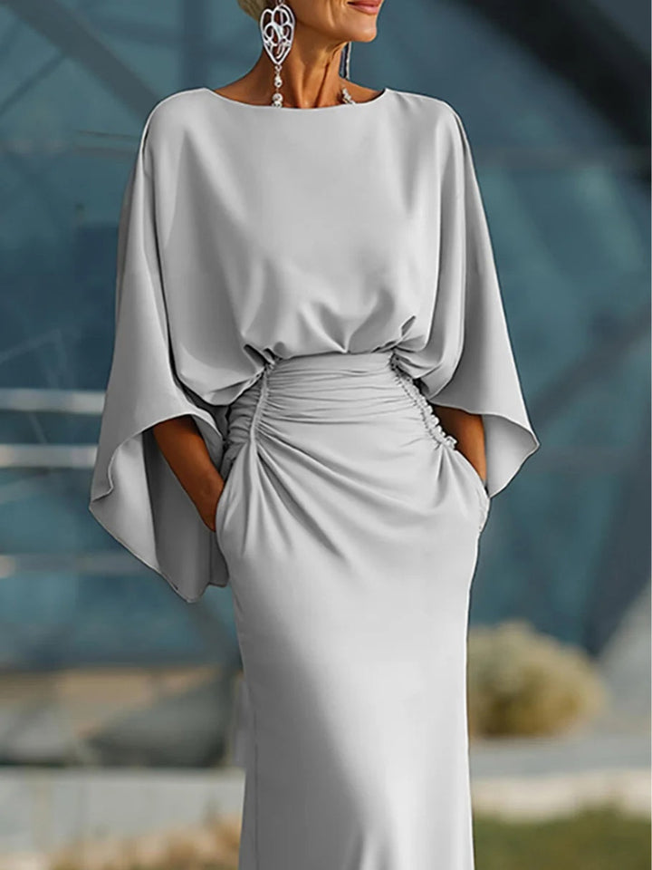 Close-up of silver dress highlighting wide sleeves and ruched waist, worn by a model in front of an architectural background.