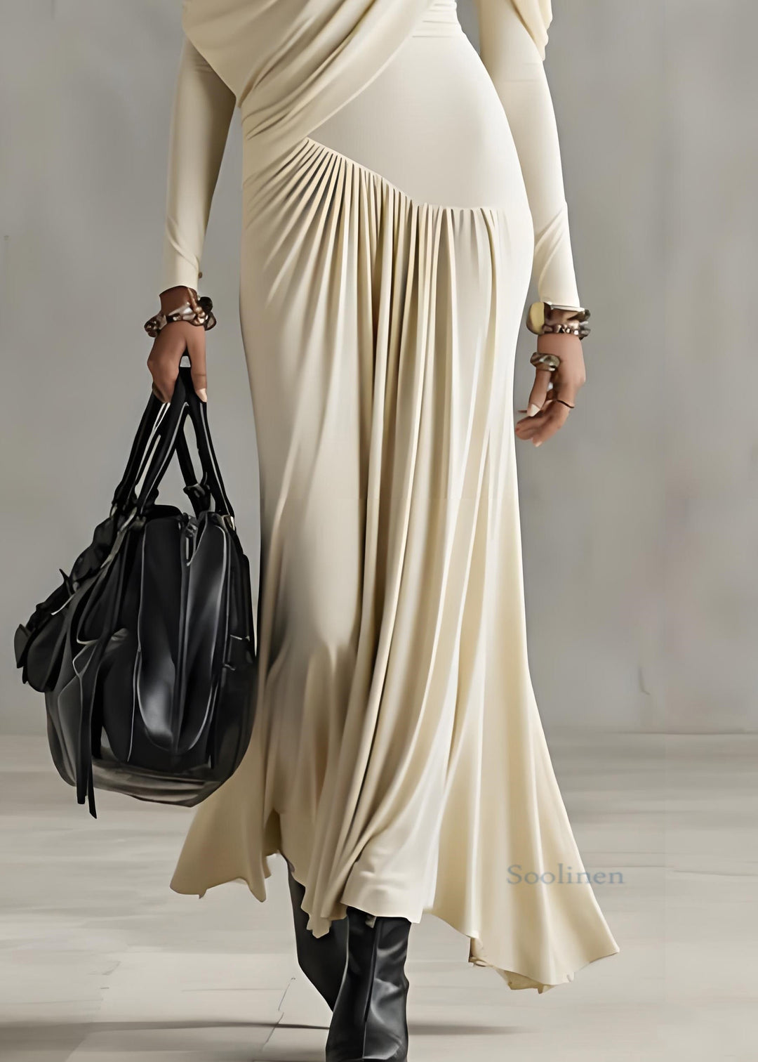 Lower view of apricot long dress with draped details, holding a black bag in a minimalist indoor setting.