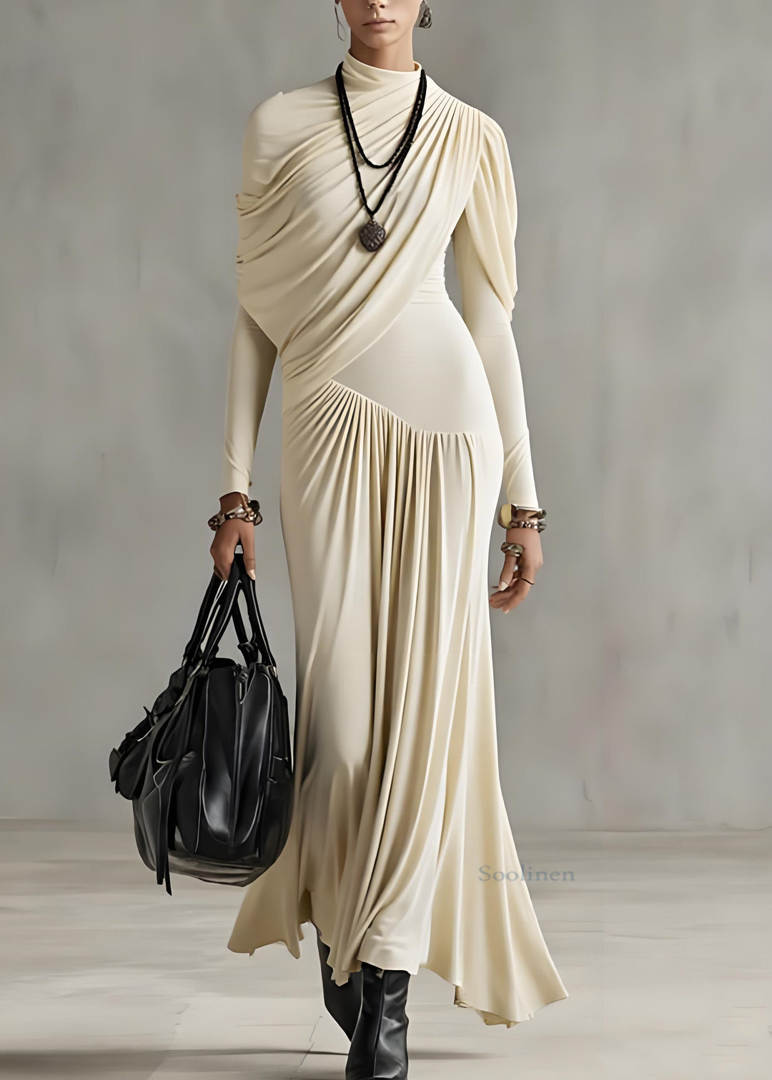 Woman in elegant apricot long dress, draped style, with a black bag in a sleek indoor space.