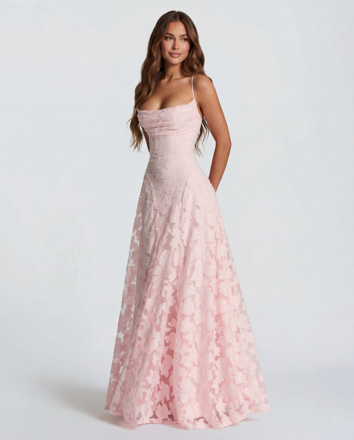 Model wearing a light pink maxi dress with thin straps and floral pattern, set against a plain studio background.