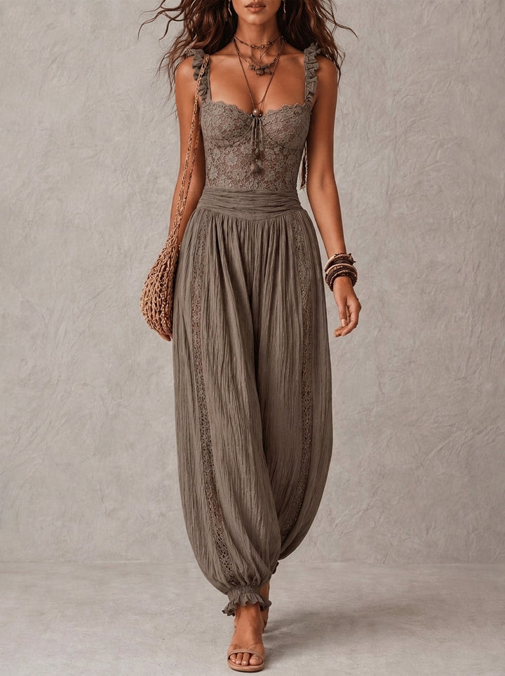 Woman wearing a lace top and pleated pants in a neutral tone, paired with a woven bag, multiple bracelets, and open-toe sandals in a studio setting.