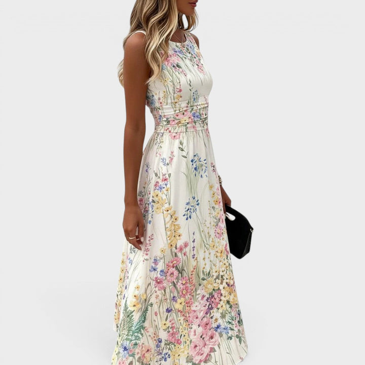 Side pose of model in sleeveless, floral midi dress with fitted waist, holding clutch. Neutral background.