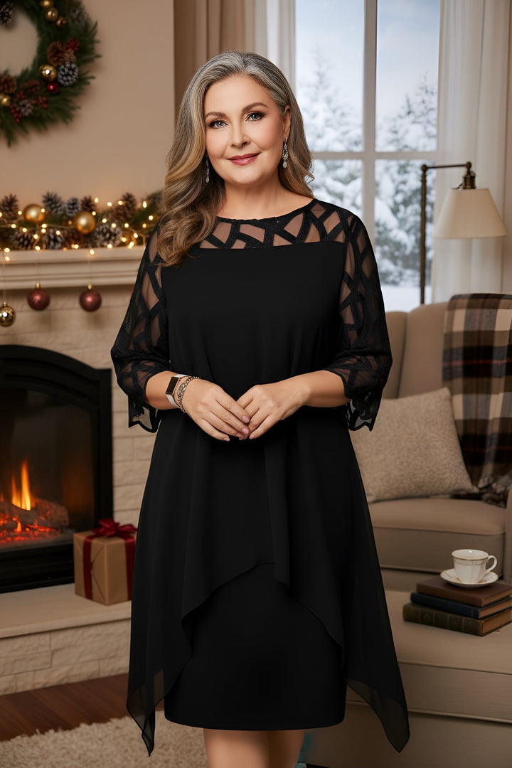 Woman in elegant black dress with lace sleeves, standing indoors by decorated fireplace.