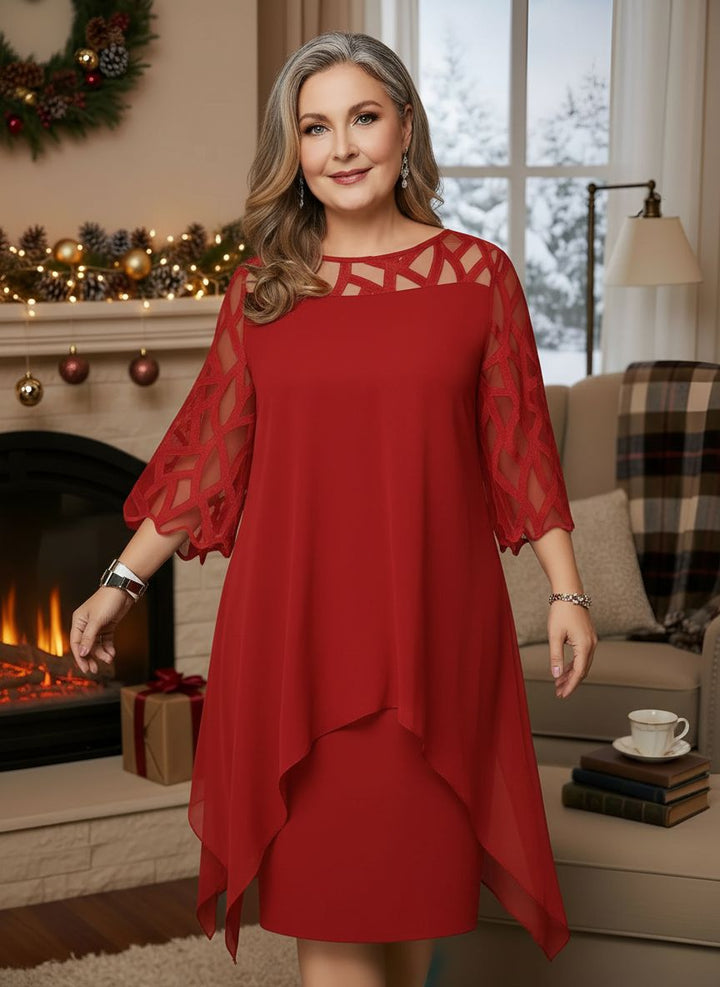 Woman in elegant red dress with lace sleeves, standing indoors by decorated fireplace.