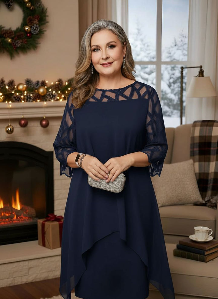 Woman in elegant navy blue dress with lace sleeves, standing indoors by decorated fireplace.