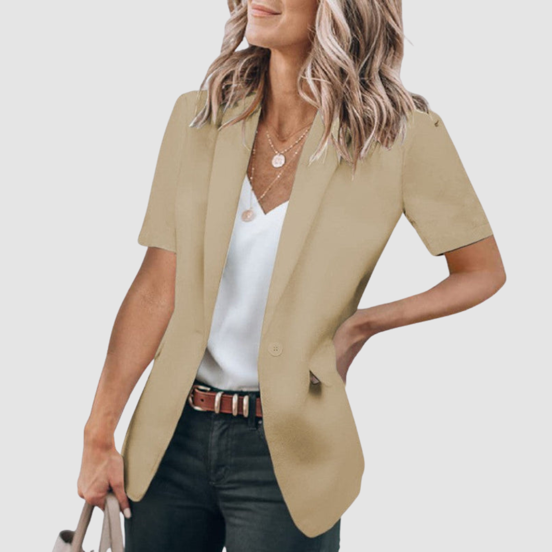 Khaki short-sleeve blazer worn by person with wavy hair, white top, and jeans; holding a beige handbag against a plain background.