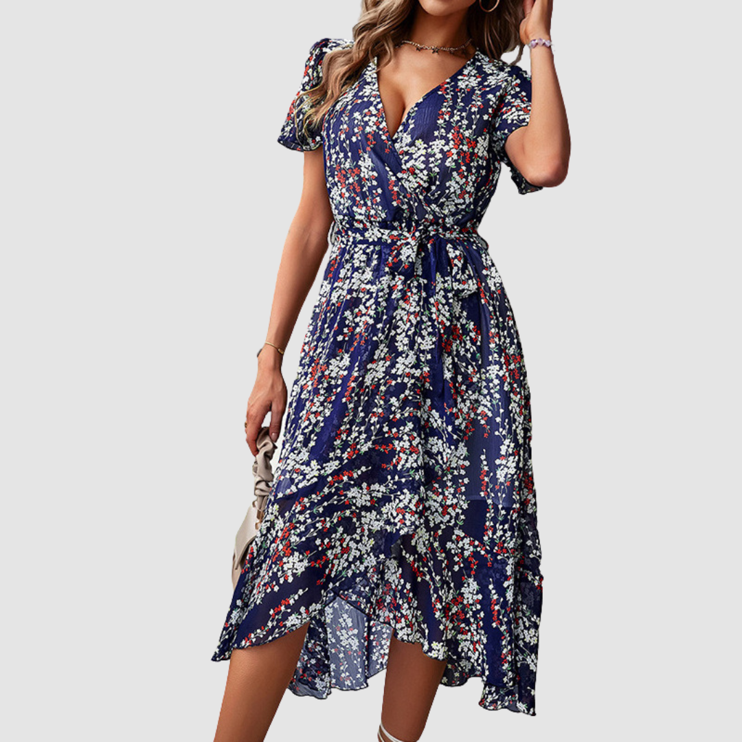 Woman wearing a blue floral printed dress with petal sleeves, tied at the waist, standing in a studio setting.