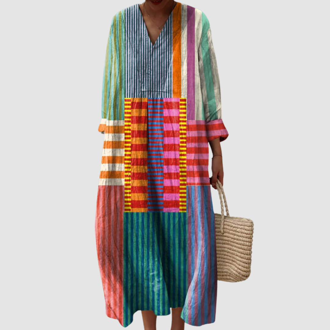 Colorful geometric dress with vertical stripes and patterns in vibrant shades, held by a person holding a woven bag against a plain background.