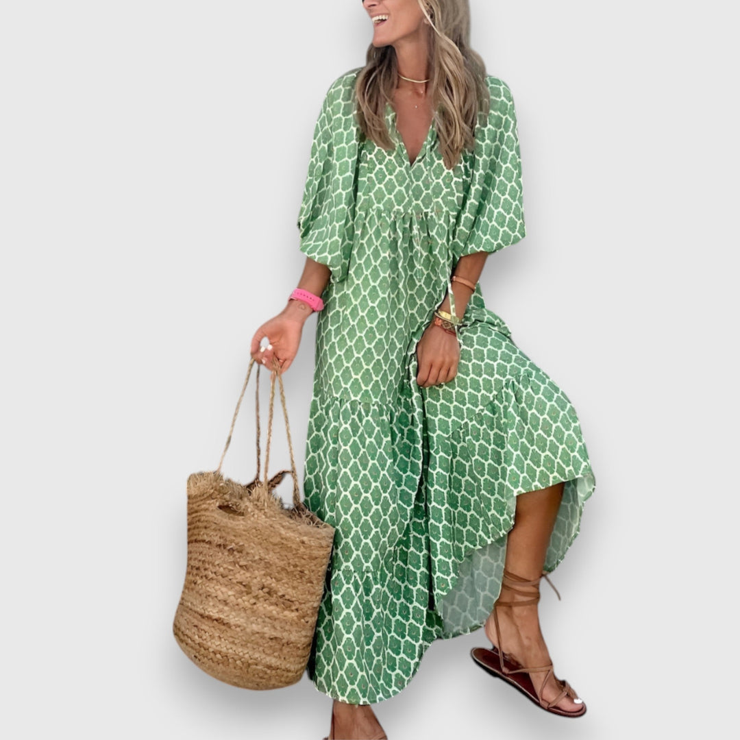 Woman in green geometric-patterned dress, holding large woven tote, on plain background.