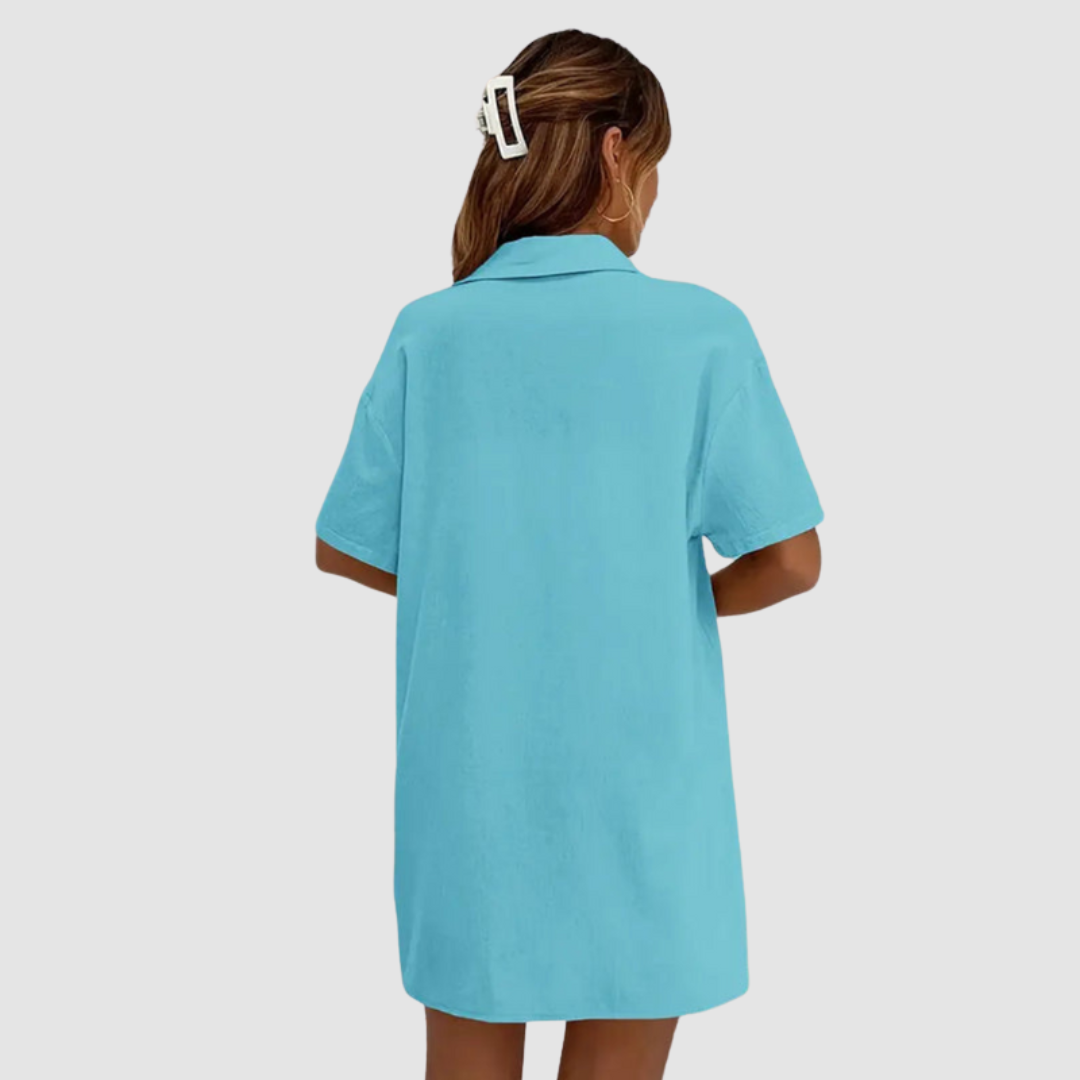 Back view of woman in blue button-up dress, hair clipped, against a studio background.