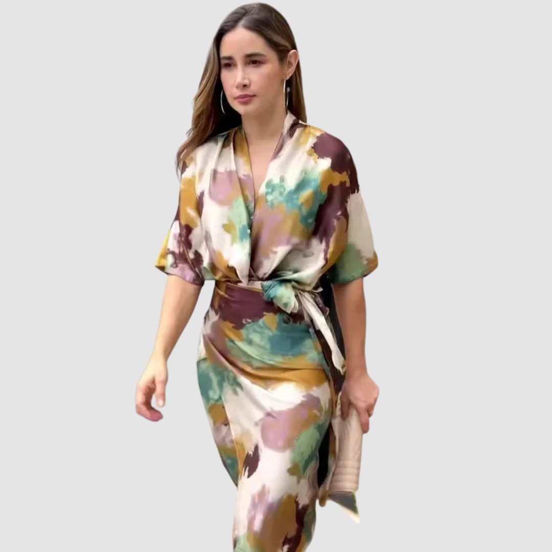 Woman wearing elegant satin dress with abstract print in earth tones, walking on a light gray background.