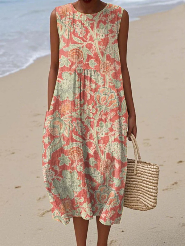 Woman wearing a floral midi dress with pastel pink and green patterns, holding a woven bag on a sandy beach.