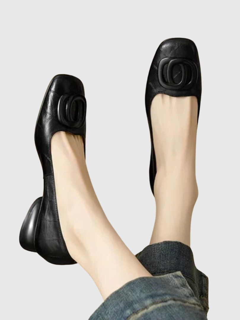Black leather flats with rounded buckle detail worn with denim, on a light background.