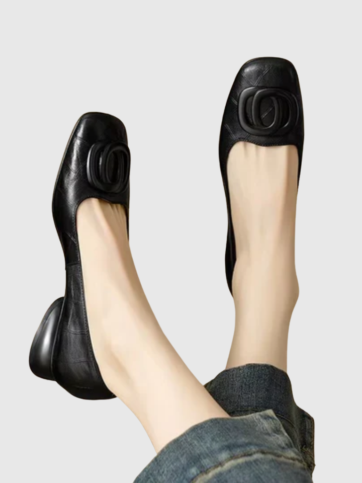 Black leather flats with rounded buckle detail worn with denim, on a light background.