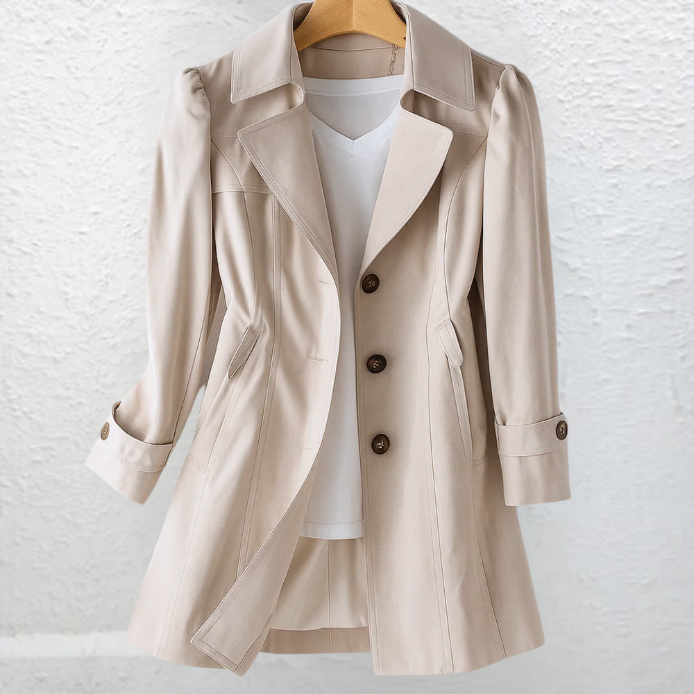 Beige coat on a hanger, displayed in front of a textured white wall.