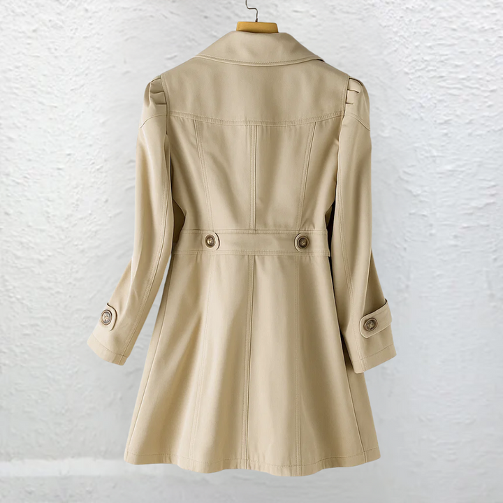 Back view of a beige coat on a hanger, in front of a textured white wall.