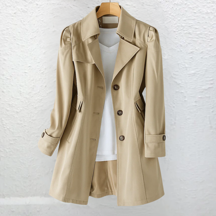 Light brown coat on a hanger, positioned before a textured white wall.