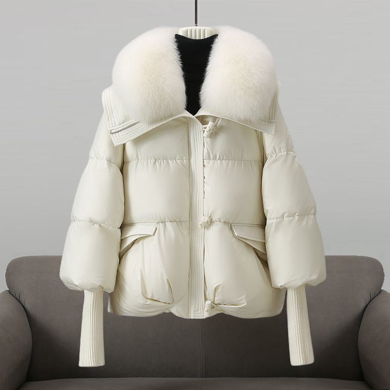 White winter jacket with an oversized fluffy white collar placed on a sofa in a studio setting.
