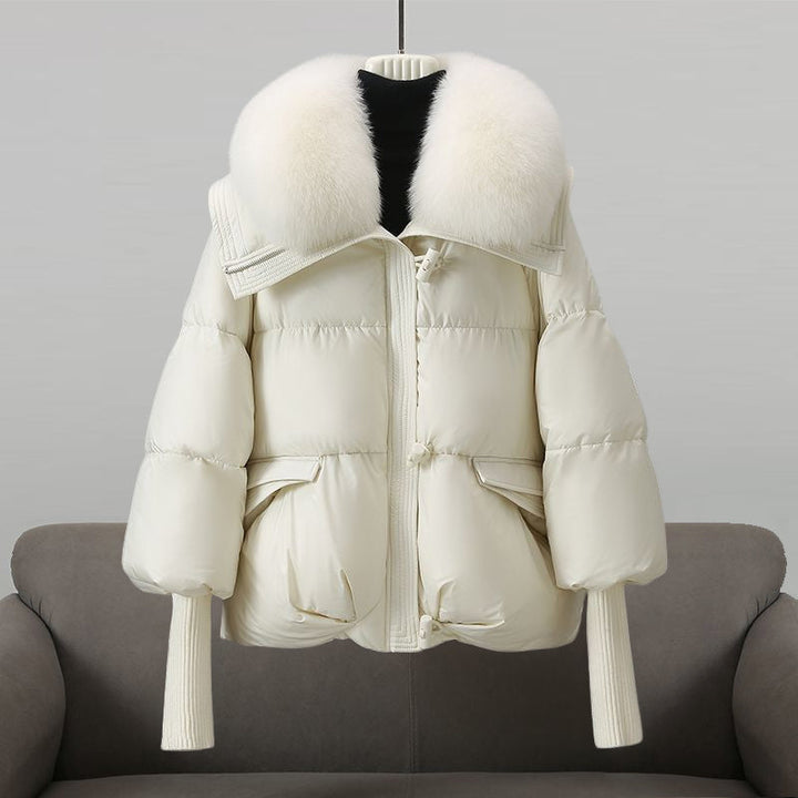 White winter jacket with an oversized fluffy white collar placed on a sofa in a studio setting.
