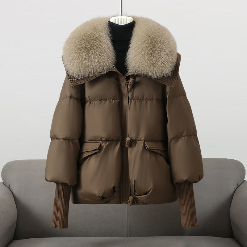 Brown winter jacket with a big fluffy beige collar showcased on a sofa in a studio environment.