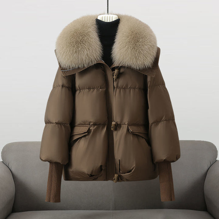 Brown winter jacket with a big fluffy beige collar showcased on a sofa in a studio environment.