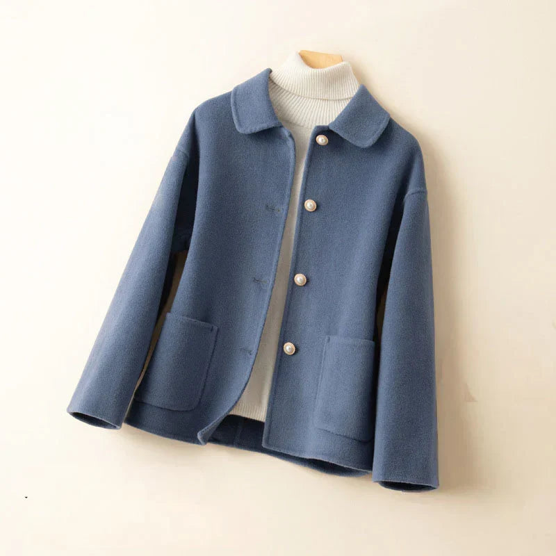 Blue pearl-accented jacket on hanger with white turtleneck in a neutral setting.