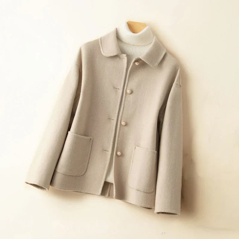 Light beige pearl-accented jacket on hanger with white turtleneck in a neutral setting.