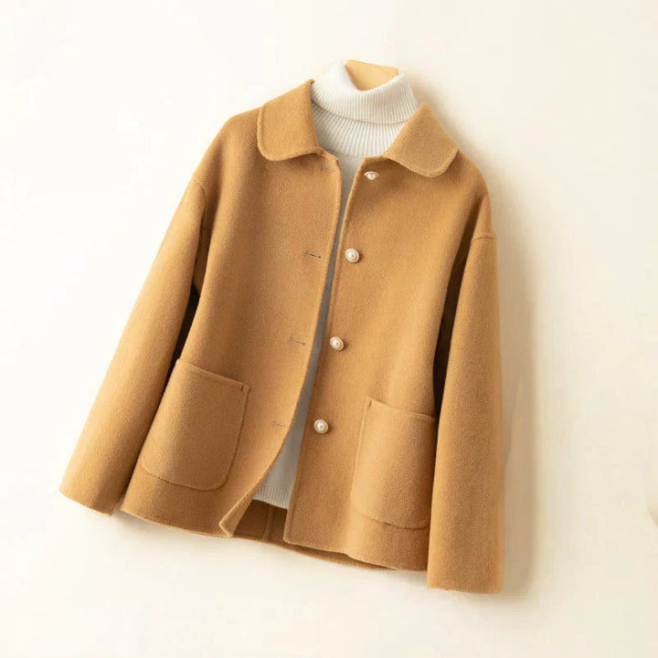 Beige pearl-accented jacket on hanger with white turtleneck in a neutral setting.