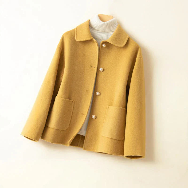 Yellow pearl-accented jacket on hanger with white turtleneck in a neutral setting.