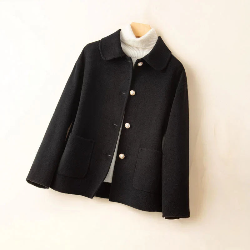 Black pearl-accented jacket on hanger with white turtleneck in a neutral setting.