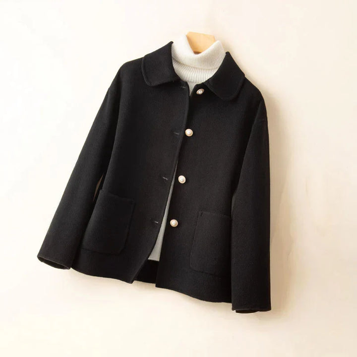 Black pearl-accented jacket on hanger with white turtleneck in a neutral setting.