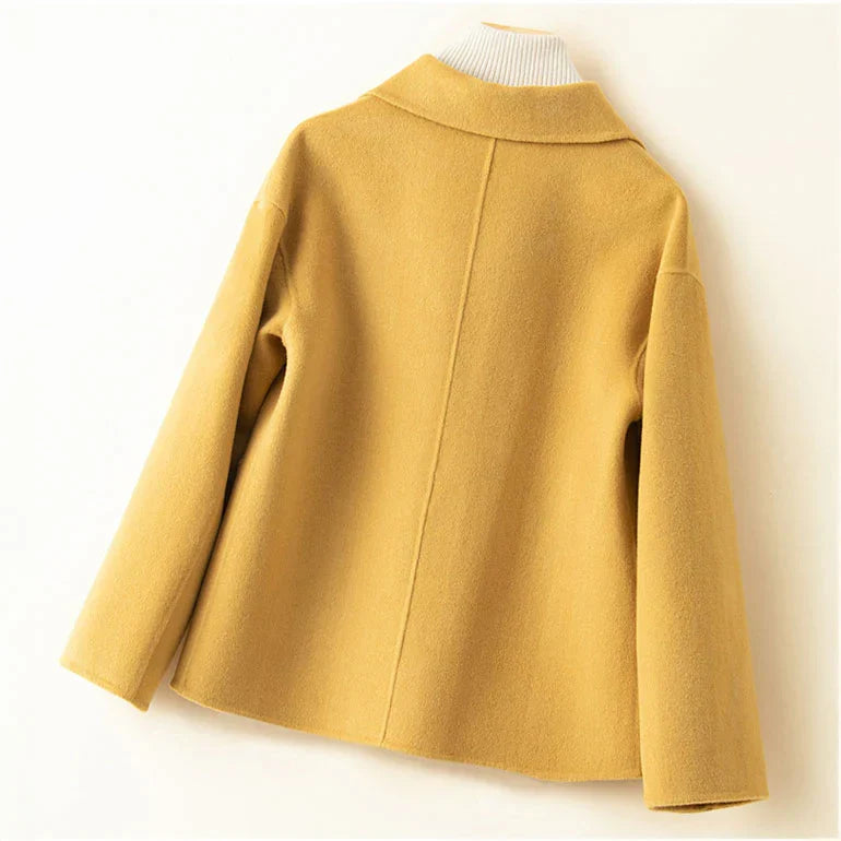 Back view of yellow jacket on hanger with white turtleneck in a neutral setting.