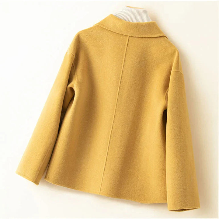 Back view of yellow jacket on hanger with white turtleneck in a neutral setting.