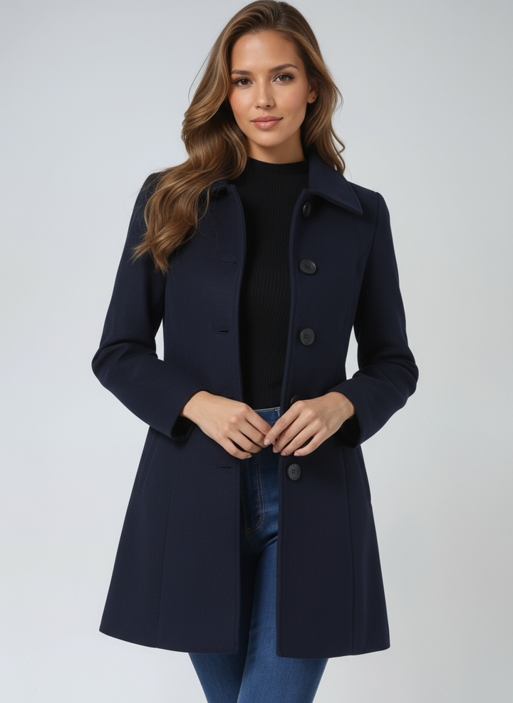 Navy blue elegant coat worn by a person, hands clasped, in a light studio setting.