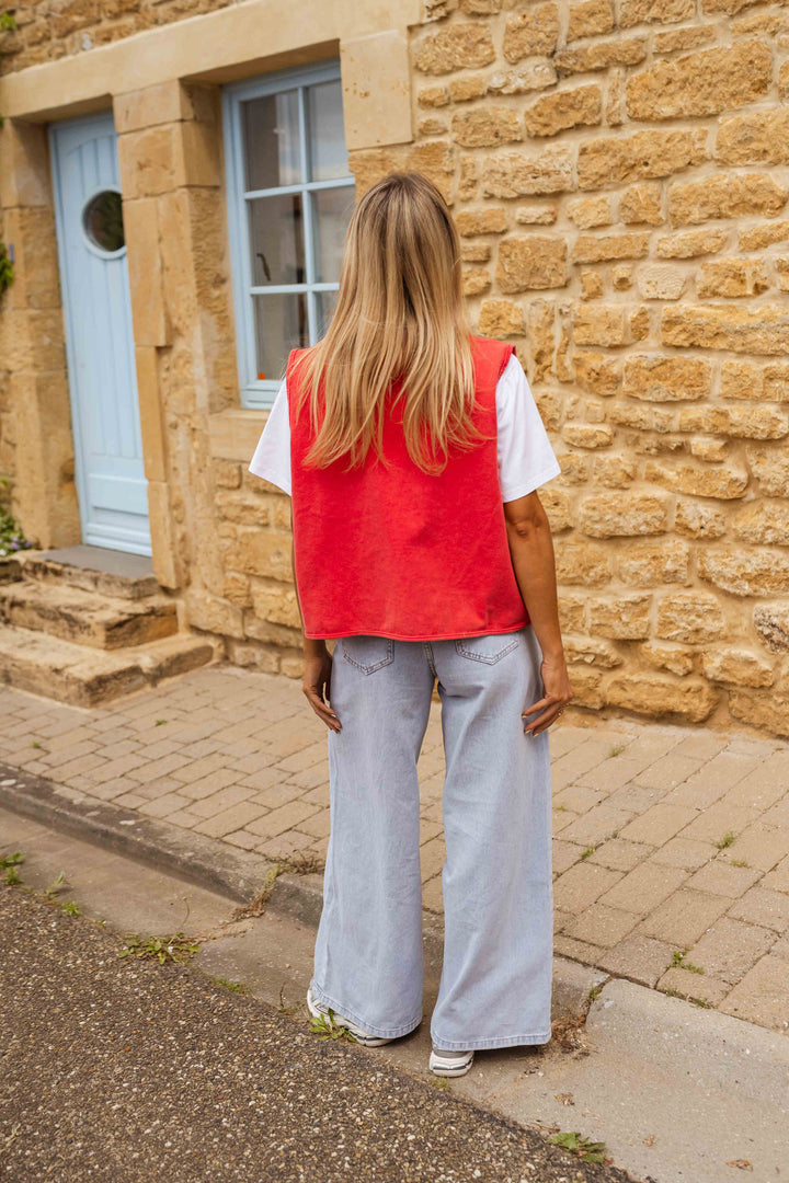 Back view of woman in red vest and light jeans, in front of stone building with blue door and window.
