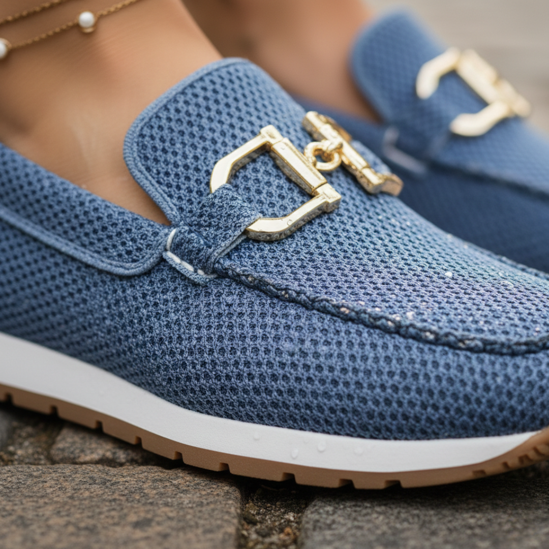 Close-up of blue orthopedic loafer with gold detail worn on a cobblestone surface.