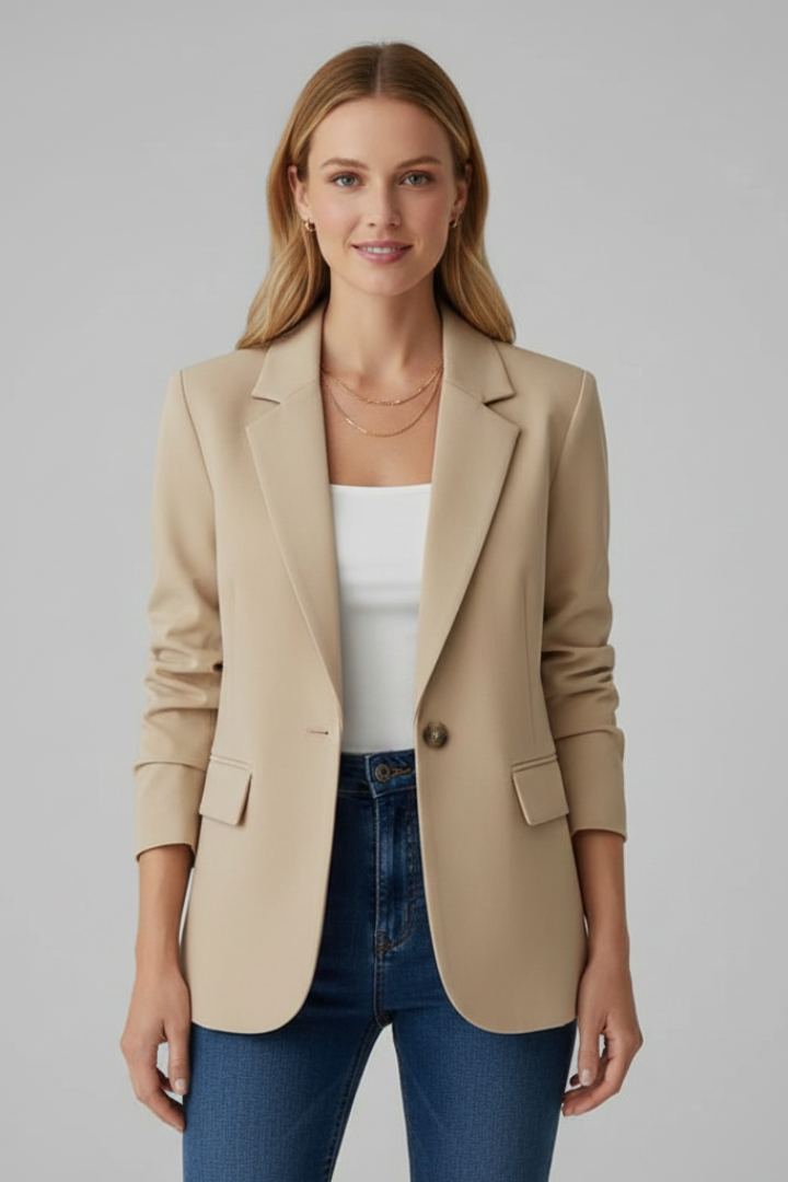Model in beige blazer, white top, jeans, simple background.