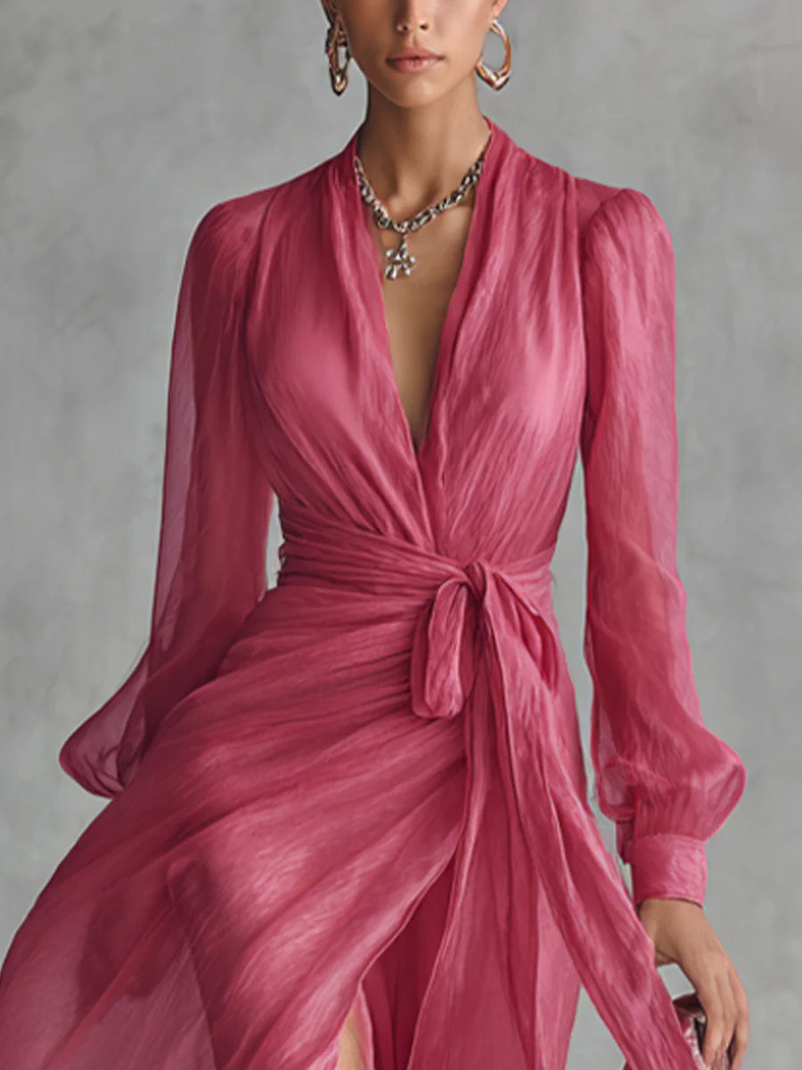 Close-up of pink long dress with a tie-waist and deep neckline, model accessorized with jewelry in a studio setting.