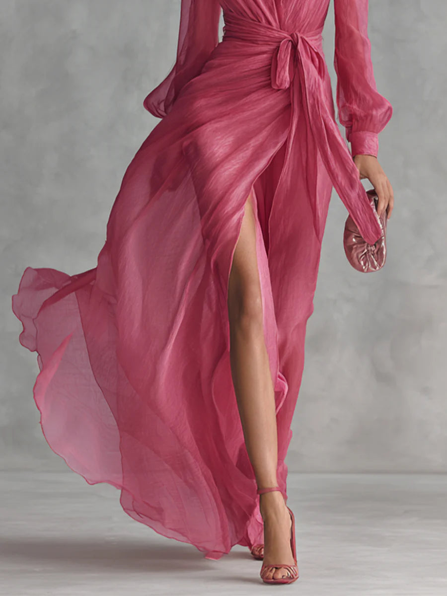 Flowing pink long dress highlighting the slit and wrap design, paired with matching heels and clutch in a studio.