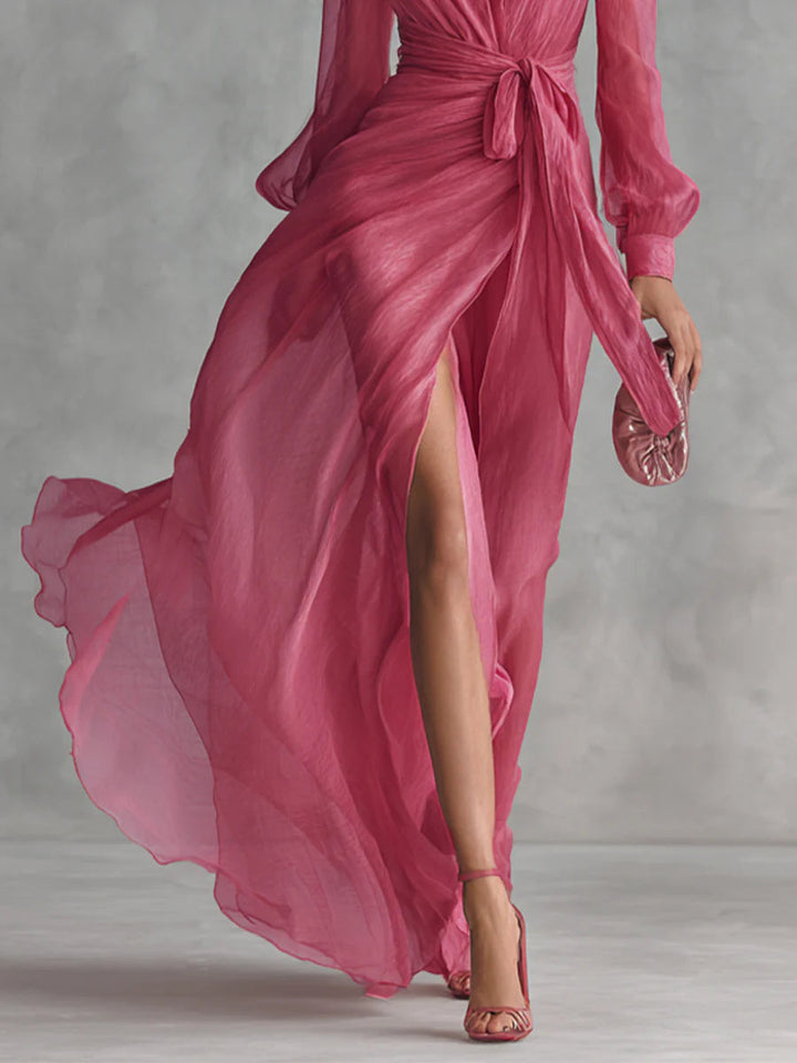 Flowing pink long dress highlighting the slit and wrap design, paired with matching heels and clutch in a studio.