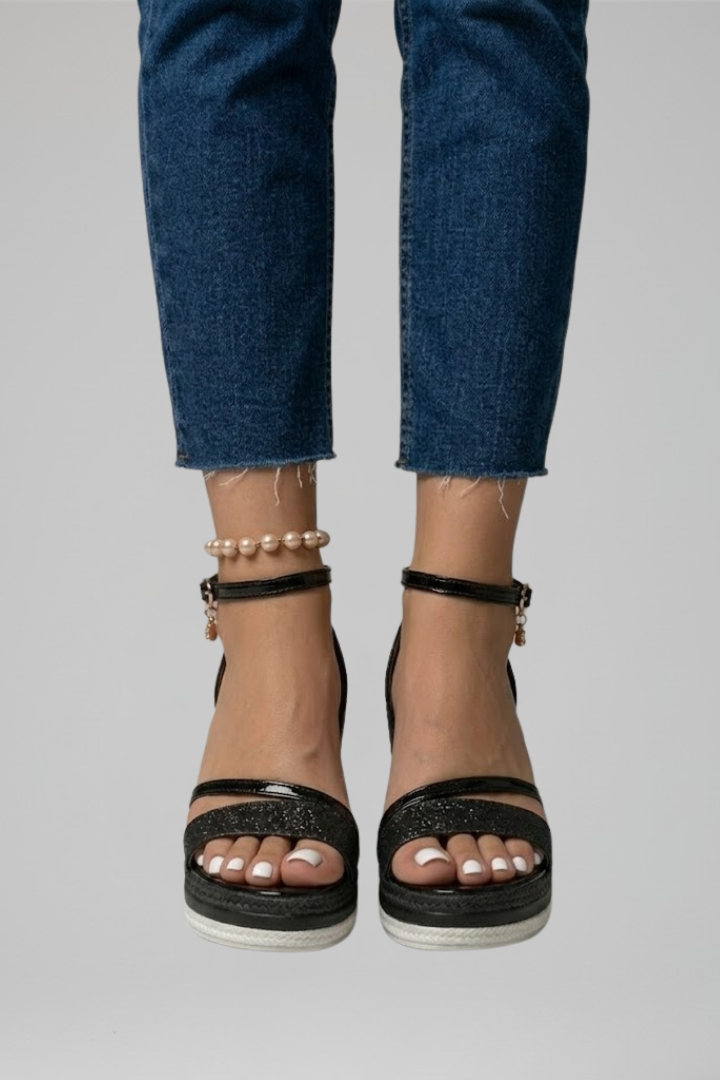 Close-up of black cushioned sandals on feet, paired with blue denim jeans in a studio.