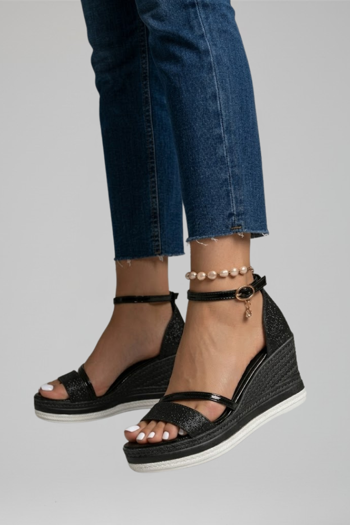 Side view of black cushioned sandals on feet, with denim jeans in a studio environment.