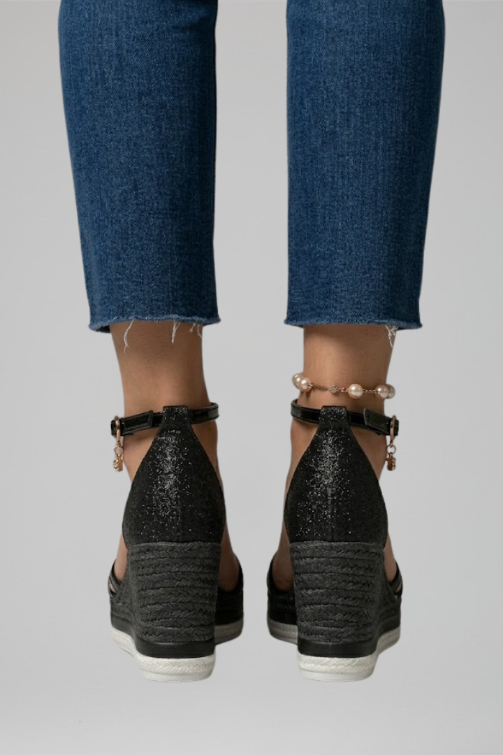 Back view of black cushioned sandals with wedge heels, paired with blue denim jeans in a studio.